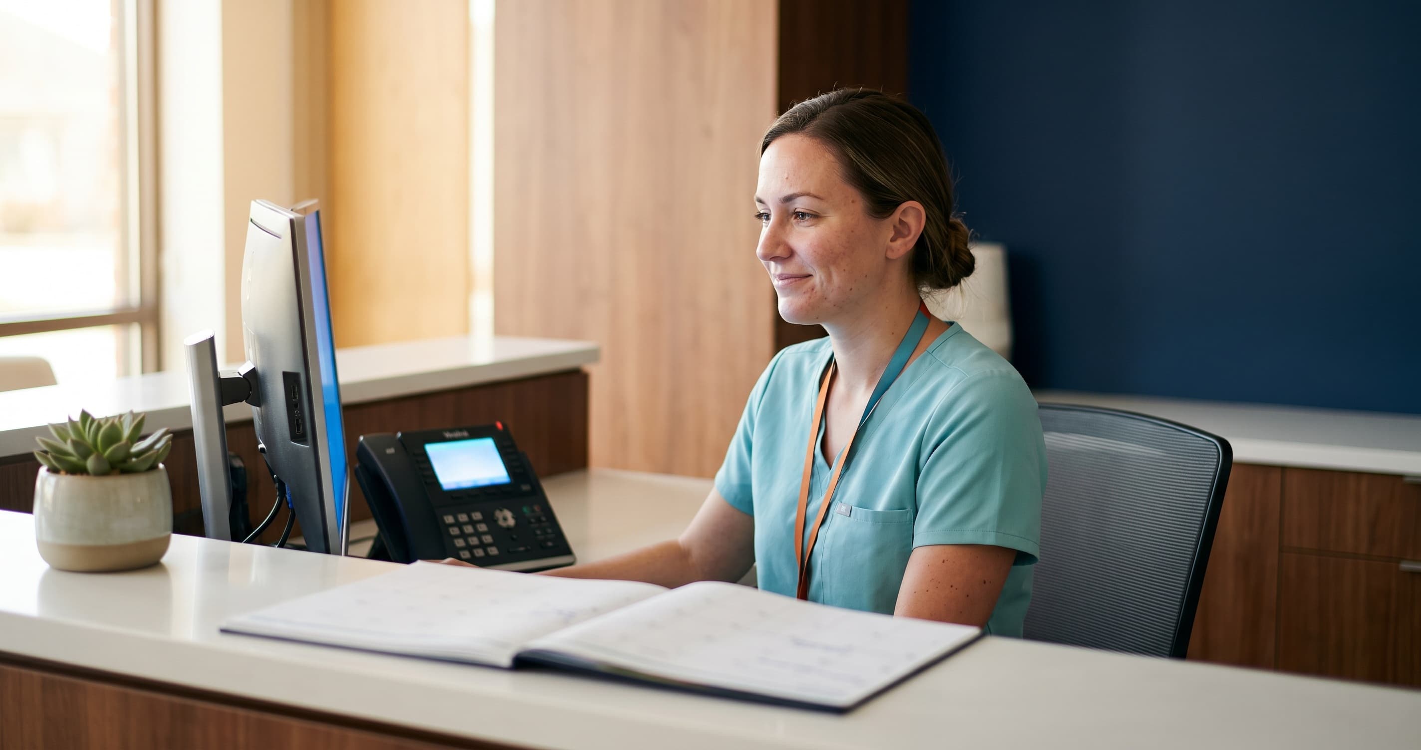 Dental receptionist at front desk smiling while AI phone system answers calls on screen, patients waiting calmly in clinic